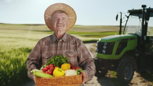 An Old Smiling Farmer is Standing By a Tractor in a Field and Looking at the Camera