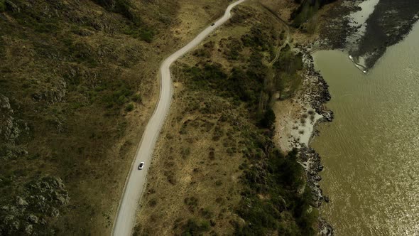 A White Car Drives Down the Road in a Mountainous Landscape