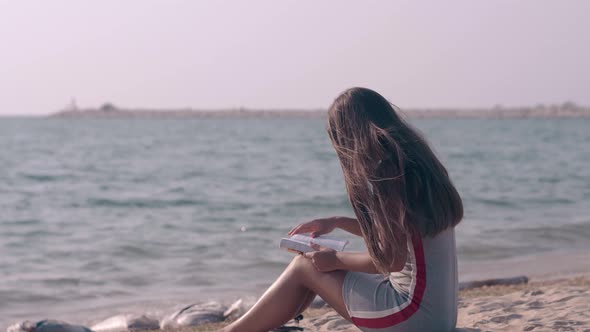 Slim Long Haired Lady Reads Book Sitting on Sandy Beach