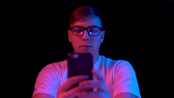 Young Man with a Smartphone. A Man Is Using a Telephone. Blue and Red Light Falls on a Man on a