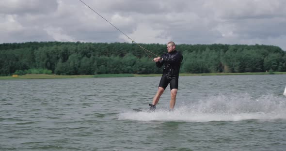Wakeboarding on the Lake Near Forest, Sportsman Surfs on Water and Does a Somersault, Ride on