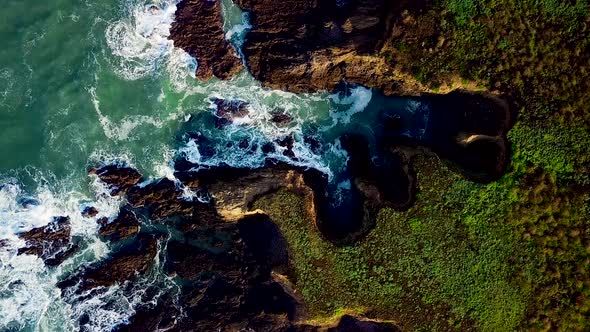 Aerial shot of waves crashing against rocky cliffs on the California coast