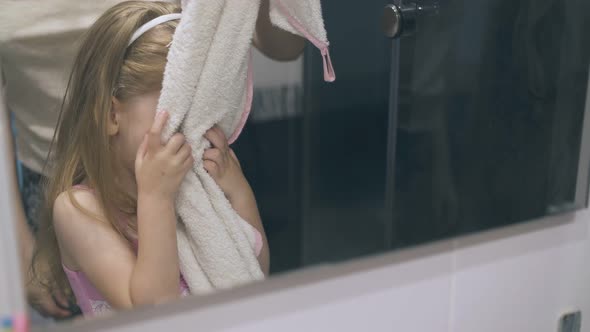 Cute Girl Wipes Face By Mother Holding Towel at Mirror