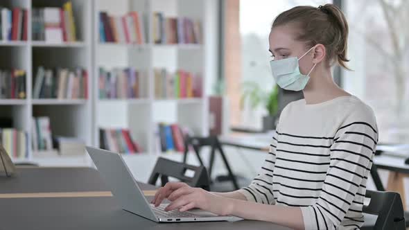 Young Woman with Face Mask Using Laptop in Library