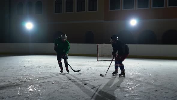 Two Sportsmen Play Hockey on a Dark Ice Arena with Spotlights
