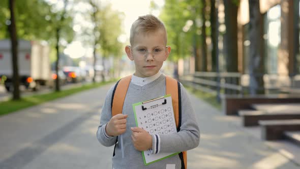 Portrait of a Schoolboy Standing on the Street Near School Holding Tests in His Hands and Carrying a