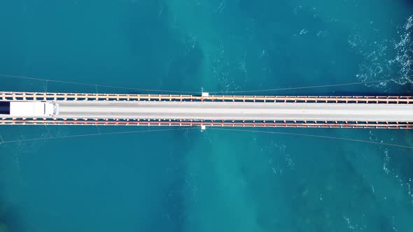 Aerial top down view of truck driving crossing over bridge. Turquoise river flowing under bridge. Pa