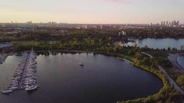 Aerial Sunset Descending Shot Of Sailboat And Marina Yacht Club Dock In Lake Bay Surrounded By Green