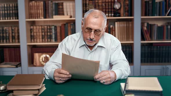 70s Elderly Man Doctor University Professor Reading Antique Letters Documents at Workplace Library