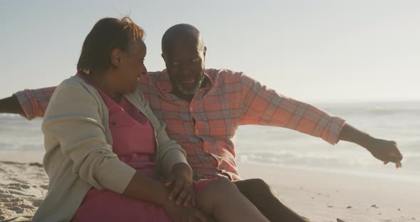 Smiling senior african american couple embracing and sitting on sunny beach