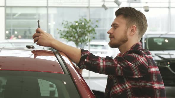 Cheerful Man Using Smart Phone Showing Car Keys To the Camera Posing at the Dealership