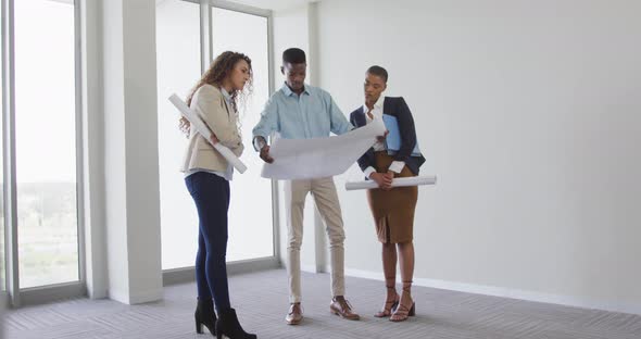 Biracial female and male architects talking and checking architects plans in modern interiors