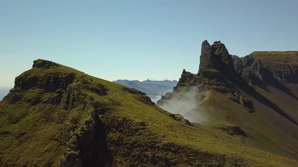 Aerial orbit of verdant steep hill summit, clouds covering mountains in background, in Djúpivogur sm