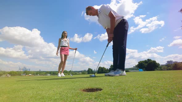 Golf Player Puts a Ball Into a Hole at a Golf Course While Woman Is Watching.