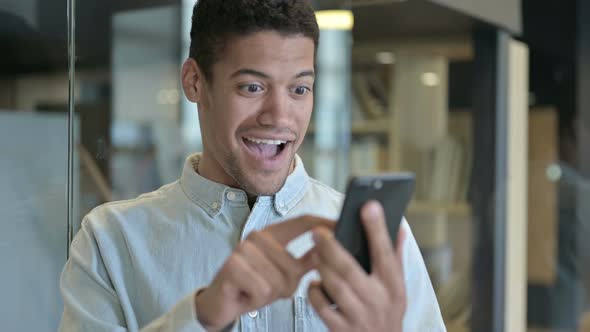 Young African Man Celebrating Success on Smartphone