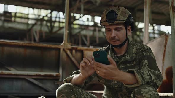 Man in Military Uniform Using Smartphone on Factory