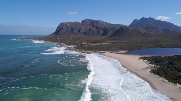 Aerial of waves breaking on pristine beach with lagoon & mountains in background, Kleinmond, South A