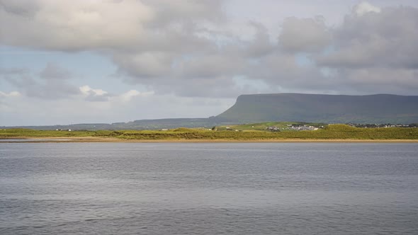 Time Lapse of sea coast of Ireland with hills in the distance and moving clouds in the sky.