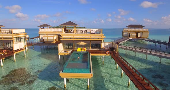 Aerial view of couple lounging by swimming pool on overwater bungalow, tropical island resort hotel.