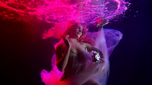 a Woman with Long Hair Floats in the Dark Water in a Stream of Bubbles. She Smiles and Plays with