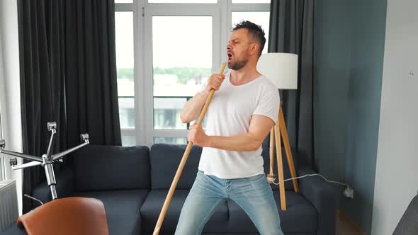 Man Cleaning the House and Having Fun Dancing and Singing with a Broom