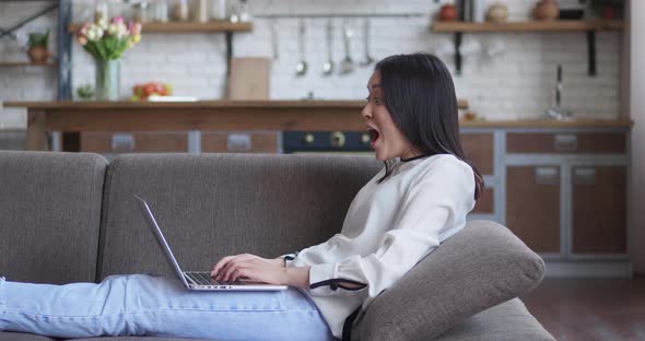 Young Asian Woman Freelancer Lying on the Couch at Home and Working on the Laptop Computer