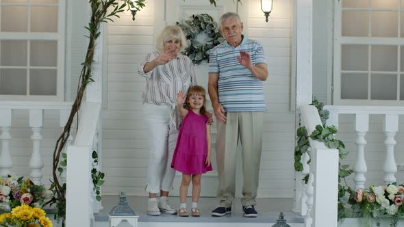 Senior Grandparens Couple with Granddaughter in Porch at Home Waving Hand, Showing Thumbs Up