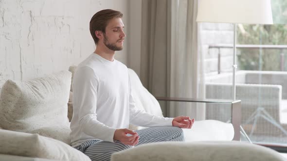 Wellness Young Man Sits on a Sofa in the Living Room and Meditates a Calm Mood Relaxing in a White