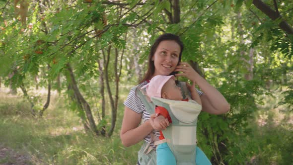 A mother with a newborn baby in a sling walk through the summer park