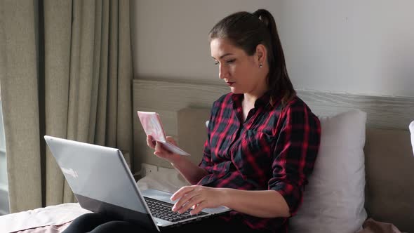 Lady with Ponytail Looks at Passport and Types on Laptop