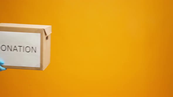 Human Hands Holding Cardboard Box with Coronavirus Donations Against Yellow Background