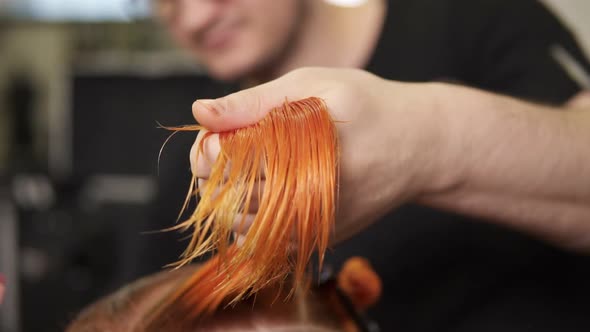 Stylish Male Hairdresser Cutting Woman's Hair in Beauty Salon While Holding a Strand of Hair in His