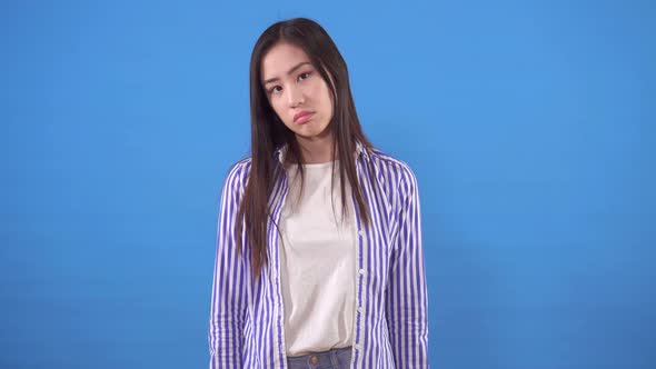 Young Asian Woman in a Shirt with a Negative Shake of Her Head on a Blue Background