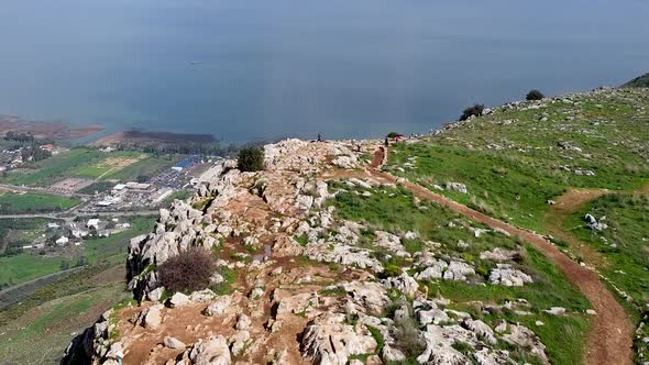 Aerial forward shot of few people on a mud trail at the Arbel cliff, Galilee sea with sun rays in th