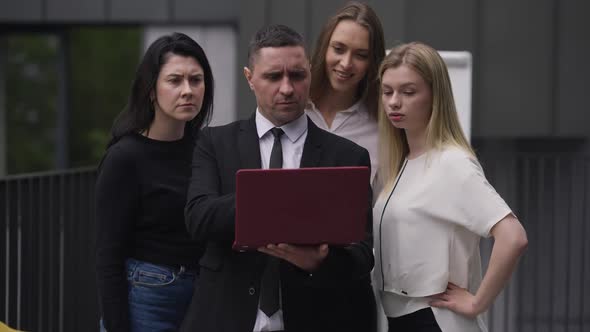 Front View of Professional Male CEO Holding Laptop Talking with Employees