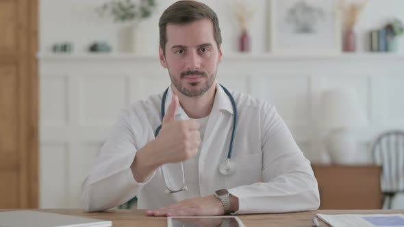 Young Doctor Showing Thumbs Up While Sitting in Clinic