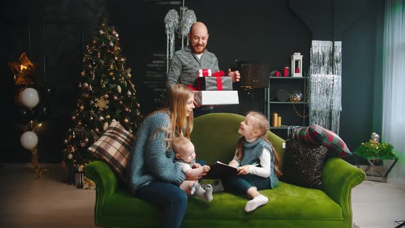 Christmas Concept - a Mom with Her Children Sitting on the Couch - Dad Comes To Them and Brings