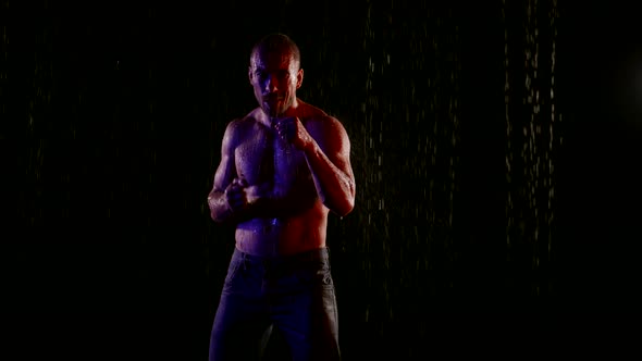 a Muscular Man with a Bare Torso Stands in the Streams of Water on a Dark Background Then Begins to