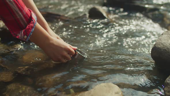 Closeup of Female Hands Filling Travel Mug with Cold Water From Mountain Stream