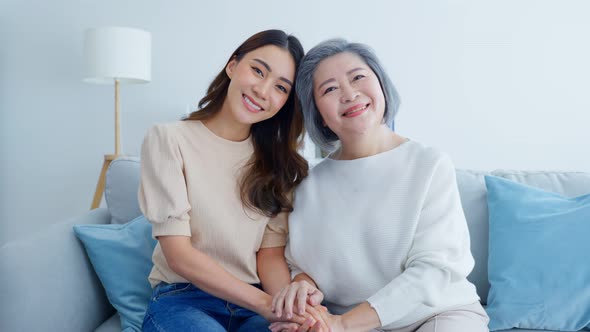 Portrait of Asian lovely family, young daughter sit with older mother in living room at home.