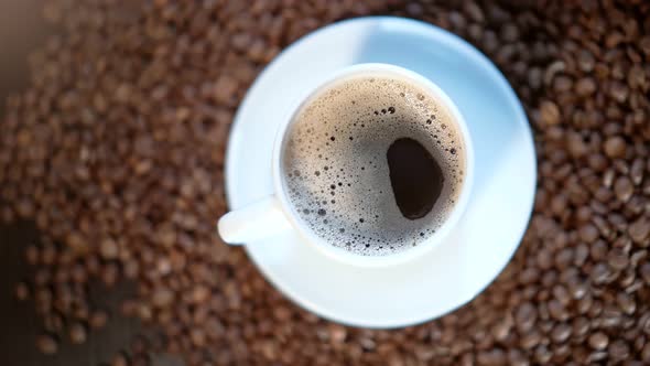 A White Coffee Mug is Standing on a Pile of Roasted Coffee Beans