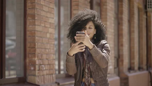 Portrait of Stylish Young African American Woman Making Selfie on Mobile Phone Then Looking Photos