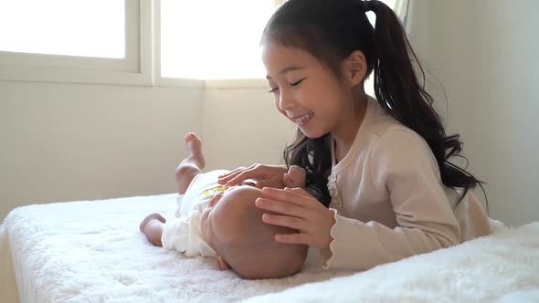 Asian Family of Cute Little Sister Touching Newborn Baby Boy Brother on Bed