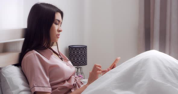 Lovely Woman is Sitting on the Bed in the Bedroom and Texting on the Phone