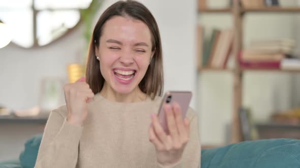 Young Woman Celebrating on Smartphone at Home