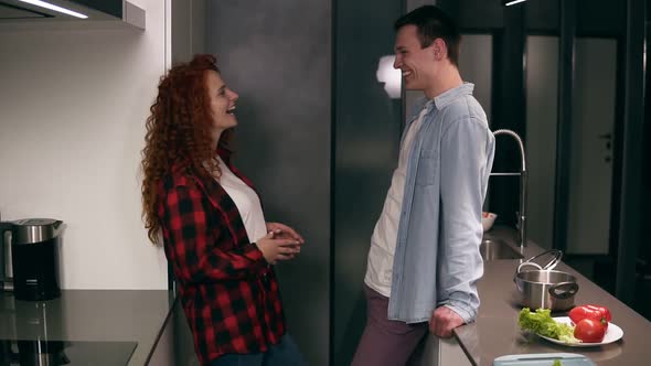 Young Happy Couple or Friends Talking in the Kitchen and Looking at Each Other