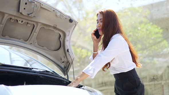 Business Asian woman using mobile phone calling for assistance after a car breakdown on street. Conc