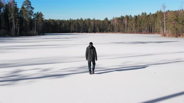 A young guy in dark clothes with short hair walks on an icy lake