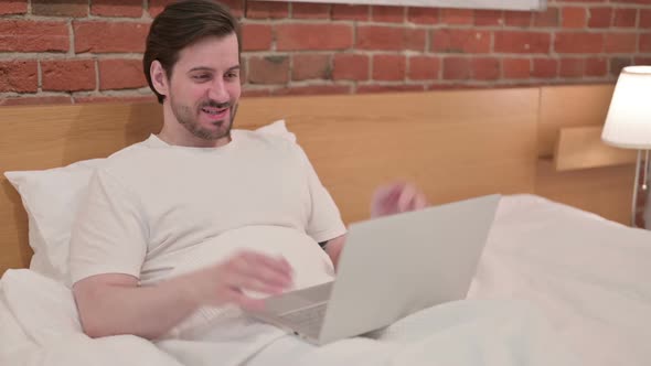 Casual Young Man Doing Video Call on Laptop in Bed
