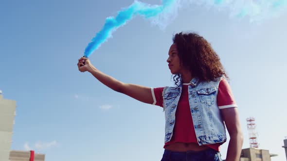 Fashionable young woman on urban rooftop using a smoke grenade